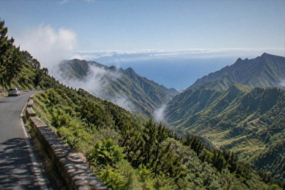 A view from a high mountain road across green terraced slopes down to a blue ocean