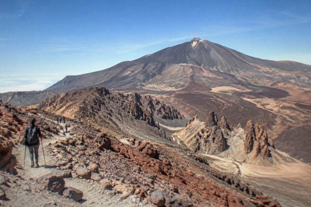 A hiker on a rocky volcanic trail high on Mount Teide with red and grey rock formations