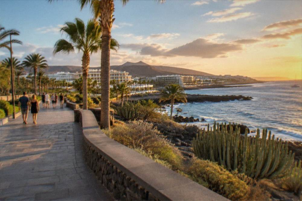 A seaside promenade in Tenerife at golden hour with palm trees and people strolling