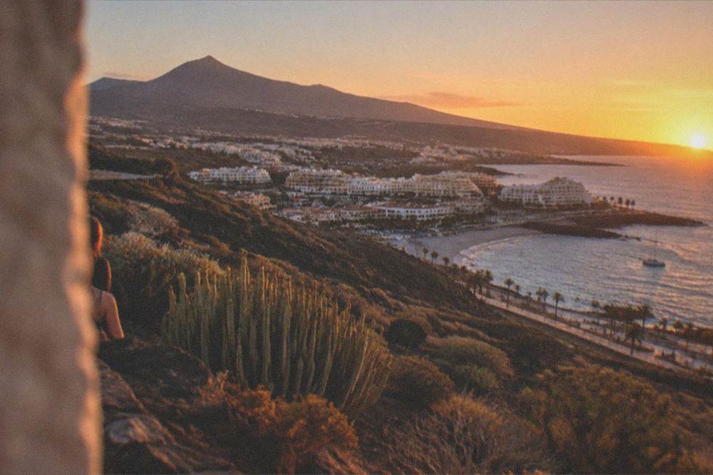 A view over a Canary island town with a volcanic peak rising in the distance at sunset