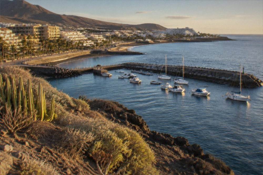 A calm Mediterranean bay with boats moored beside a stone jetty in the evening light