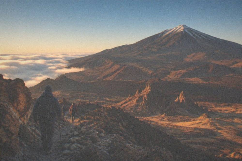 Hikers in winter clothing walking a rocky trail above the clouds on Teide