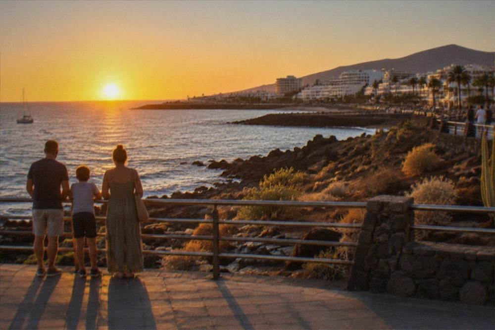 A family watching a sunset over the ocean from a promenade railing in south Tenerife