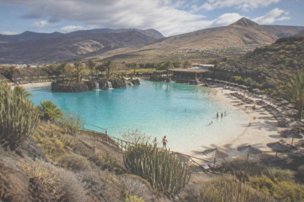 A wide water park lagoon with sun loungers and a sandy edge