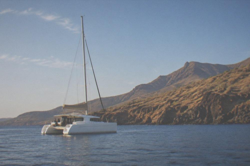A catamaran anchored in calm blue water near a volcanic coastline
