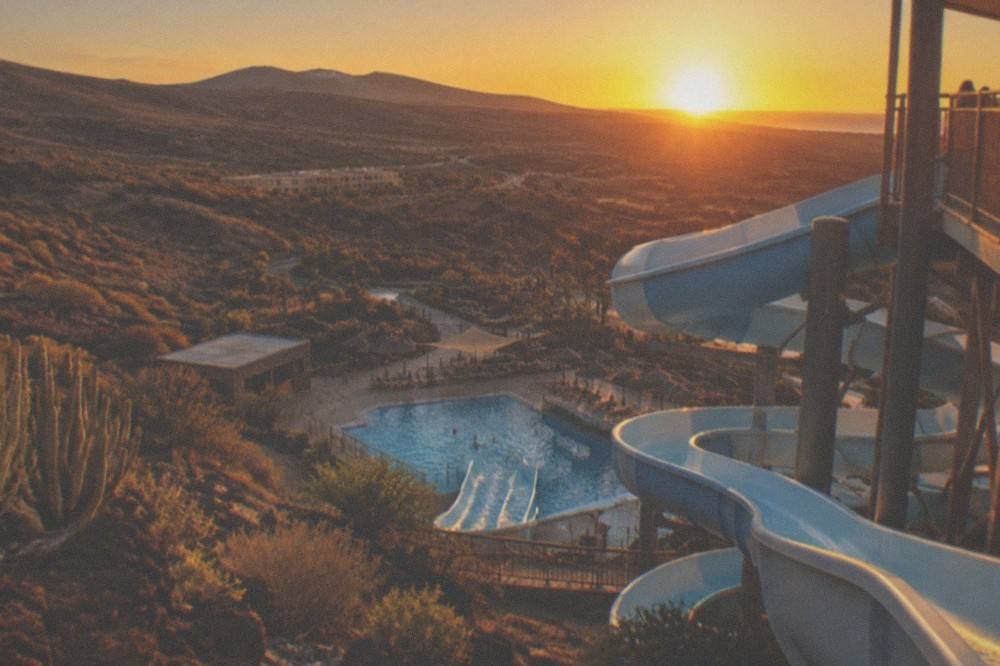 A water park slide winding down a tower towards a splash pool at sunset