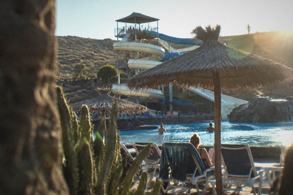 Sunbeds and thatched umbrellas along a water park pool with a slide tower behind