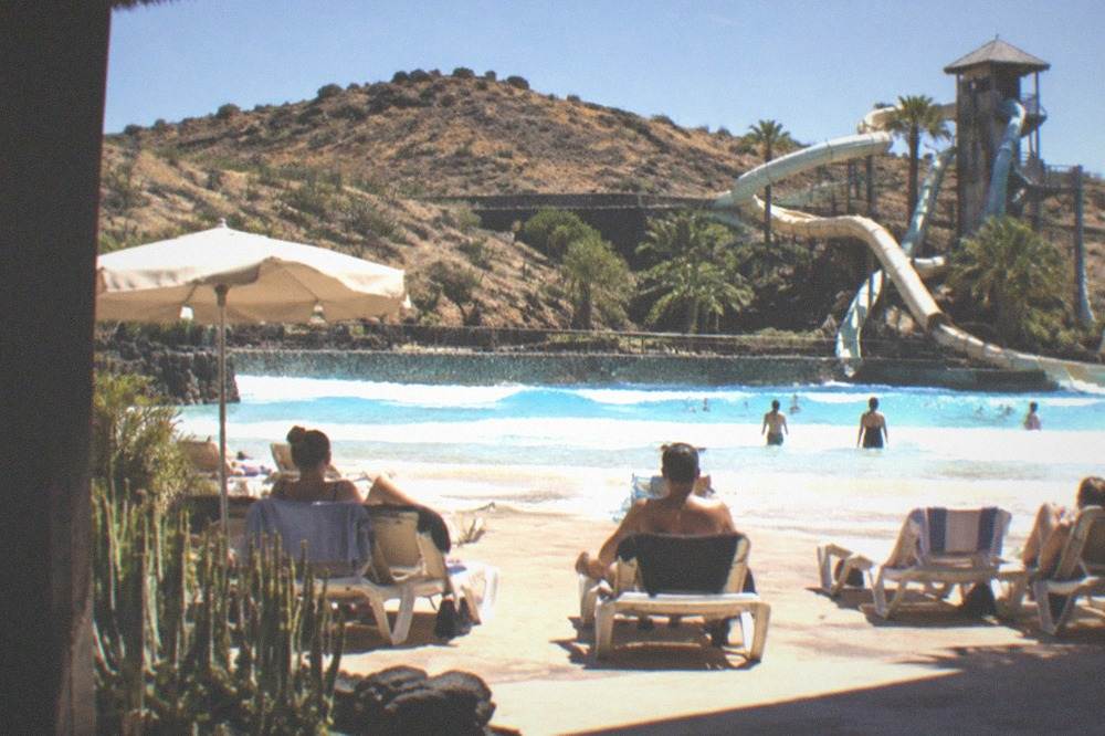People on sunbeds beside a wave pool with a slide tower in the background