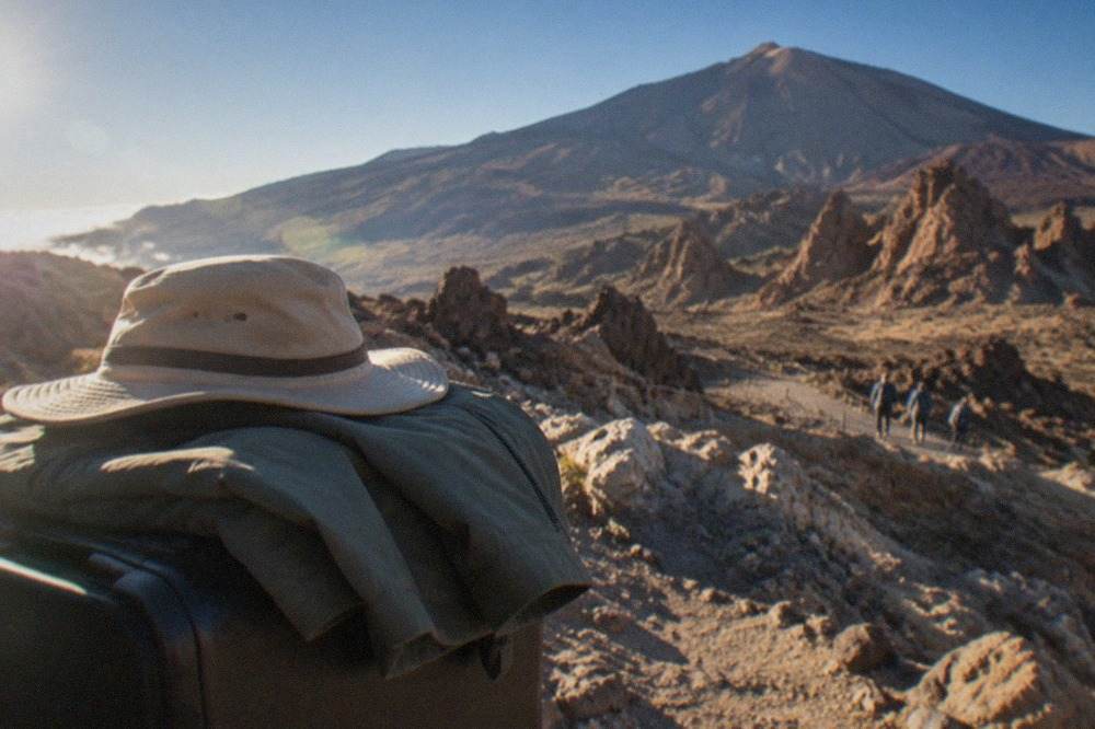 A folded jacket and a sun hat resting on a suitcase in bright island light