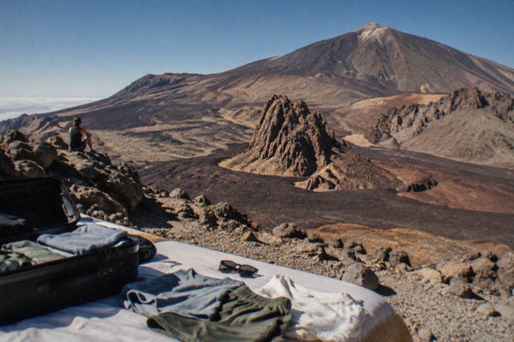 Light summer clothing and sunglasses laid out on a bed beside an open suitcase