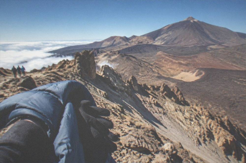 A warm jacket and gloves held against a view of a volcanic ridge above the clouds