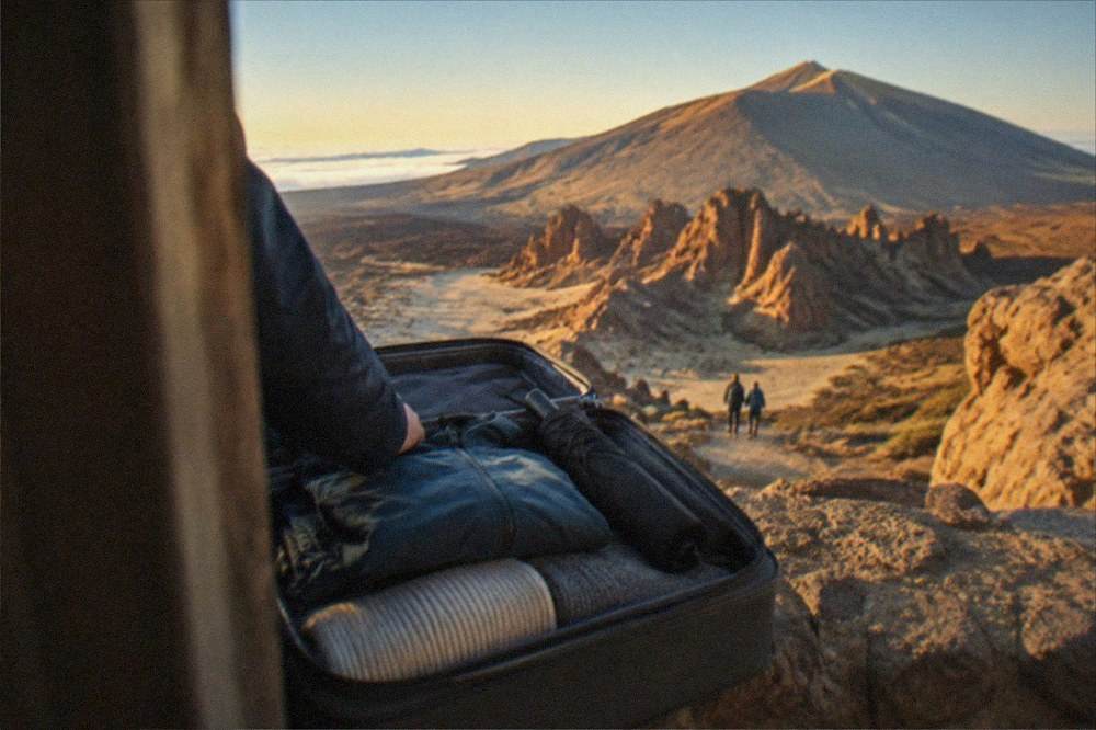 A waterproof jacket and umbrella packed above folded jumpers in a suitcase