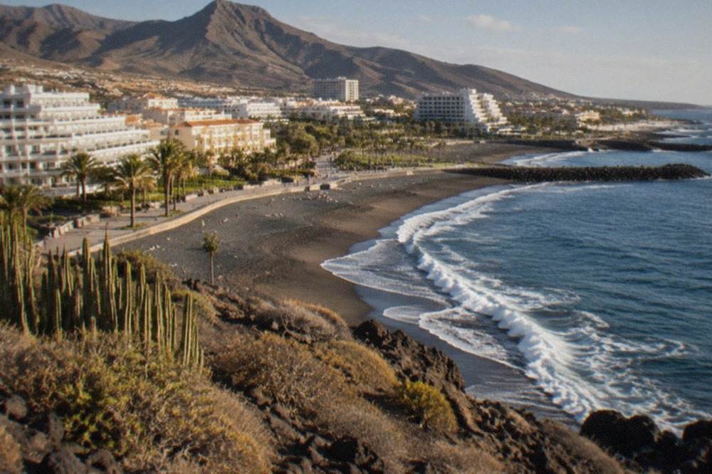 Aerial view of a Tenerife coastal resort with hotels, dark sand and Atlantic waves