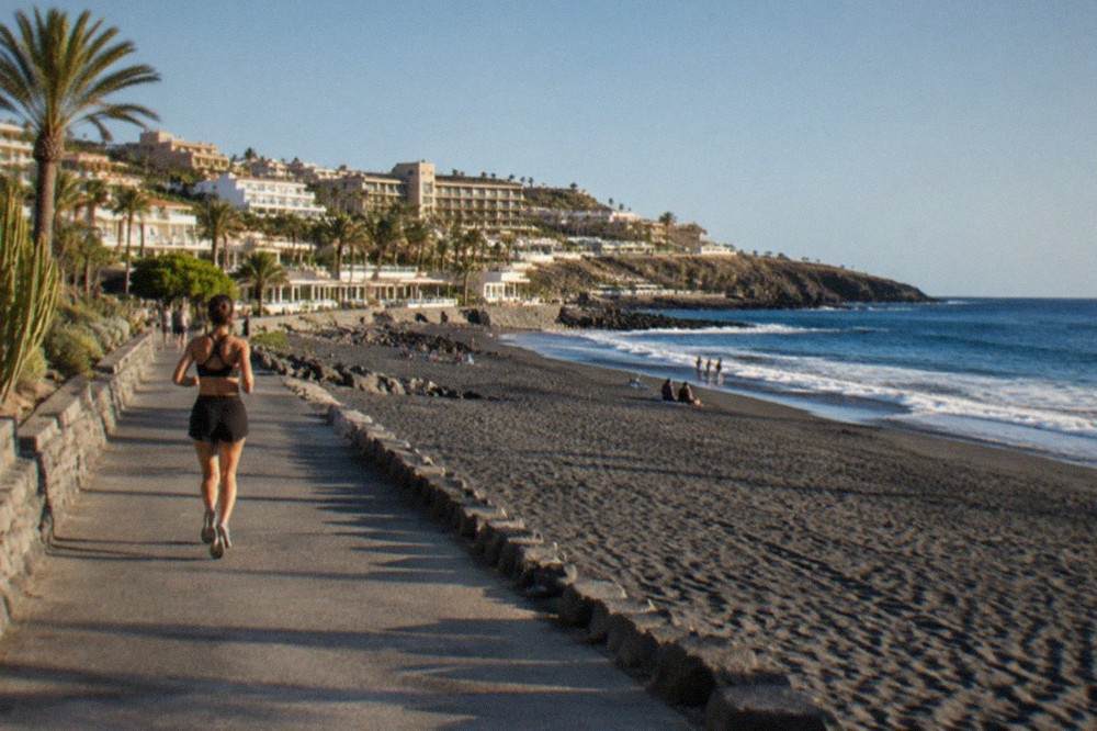 Hotels and pools above a grey sandy beach in Costa Adeje under a clear sky