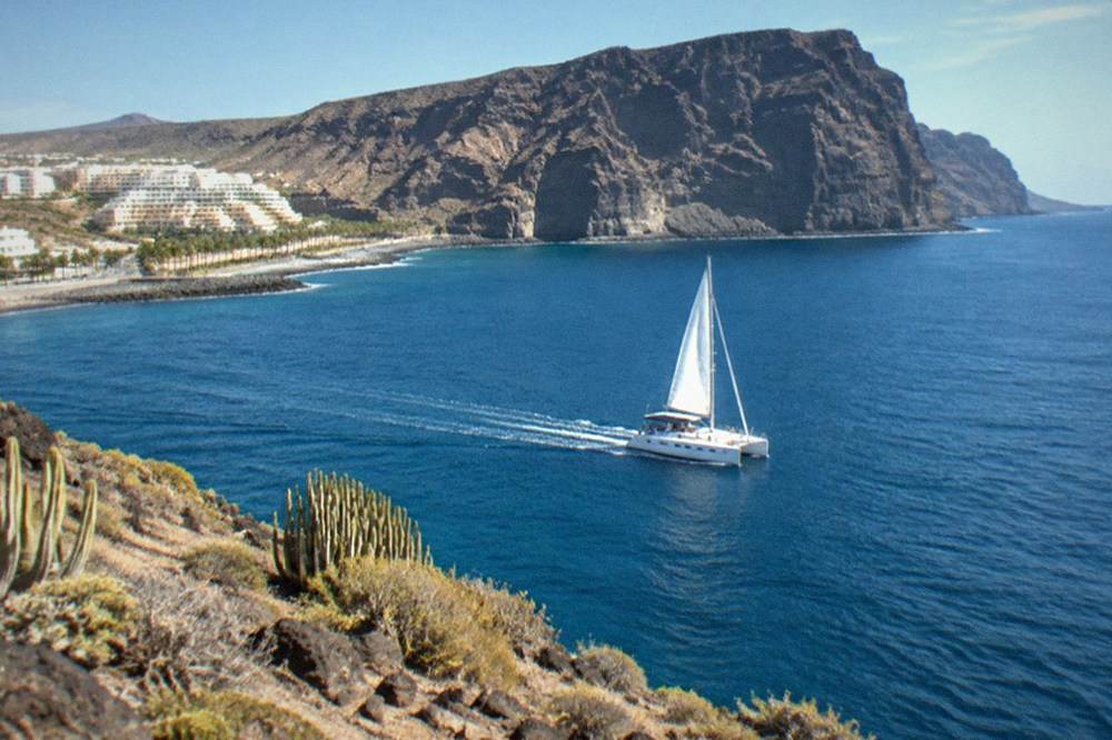 A catamaran cruising near tall dark cliffs rising from the sea