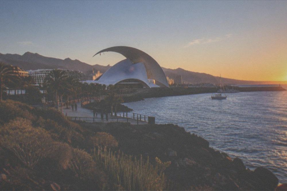 A white curved concert hall beside a harbour at dusk