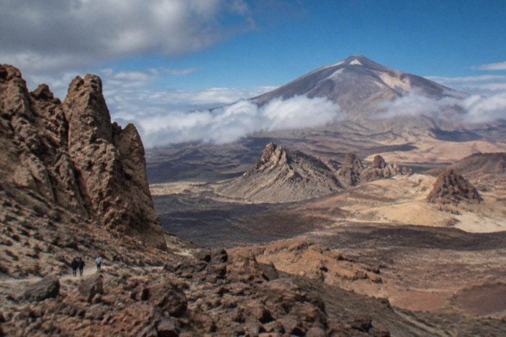 View across volcanic landscape towards Mount Teide rising above cloud in Tenerife