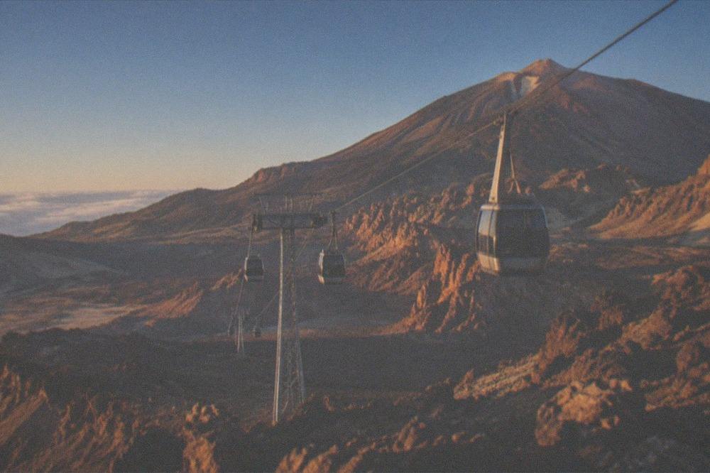 Cable car cabins ascending a rocky volcanic slope towards high peaks