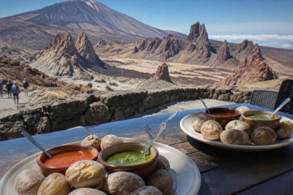 Plates of wrinkled potatoes with red and green mojo sauces on a restaurant table