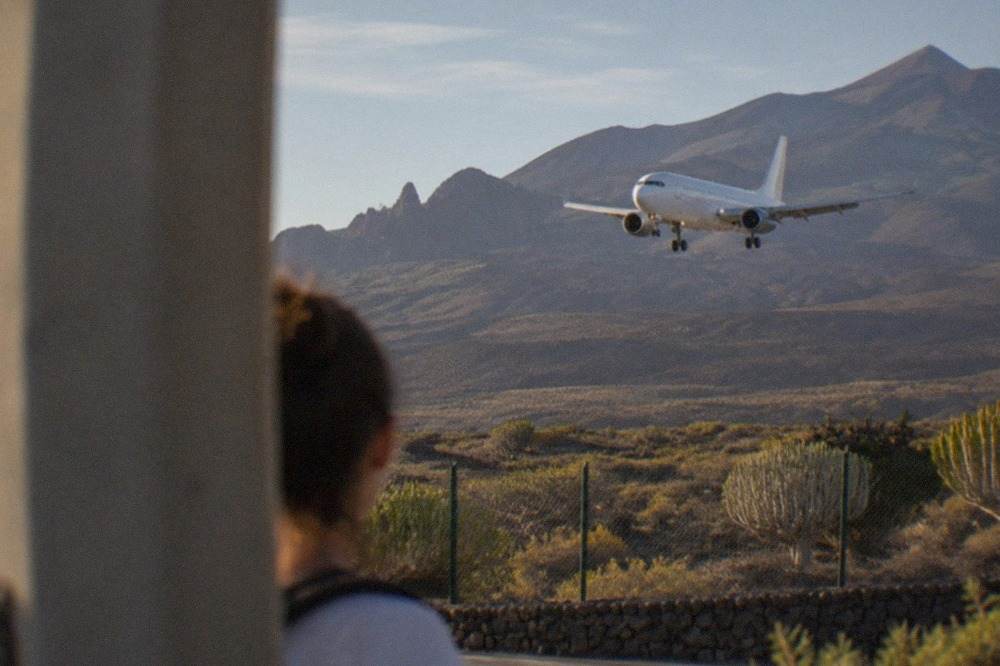 A passenger aircraft on approach over the volcanic coastline of Tenerife with mountains rising behind