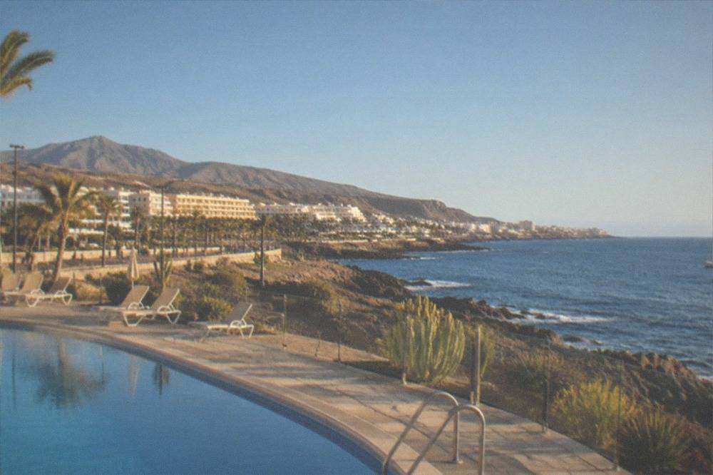 A resort swimming pool and coastline in Costa Adeje under sunshine