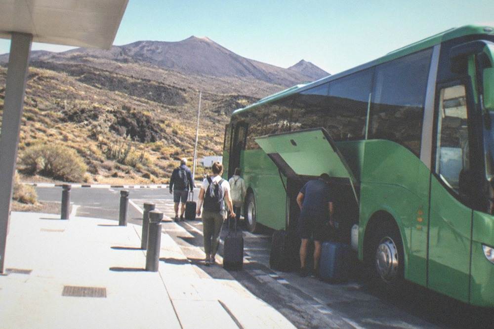 A green island bus at an airport stop with luggage being loaded