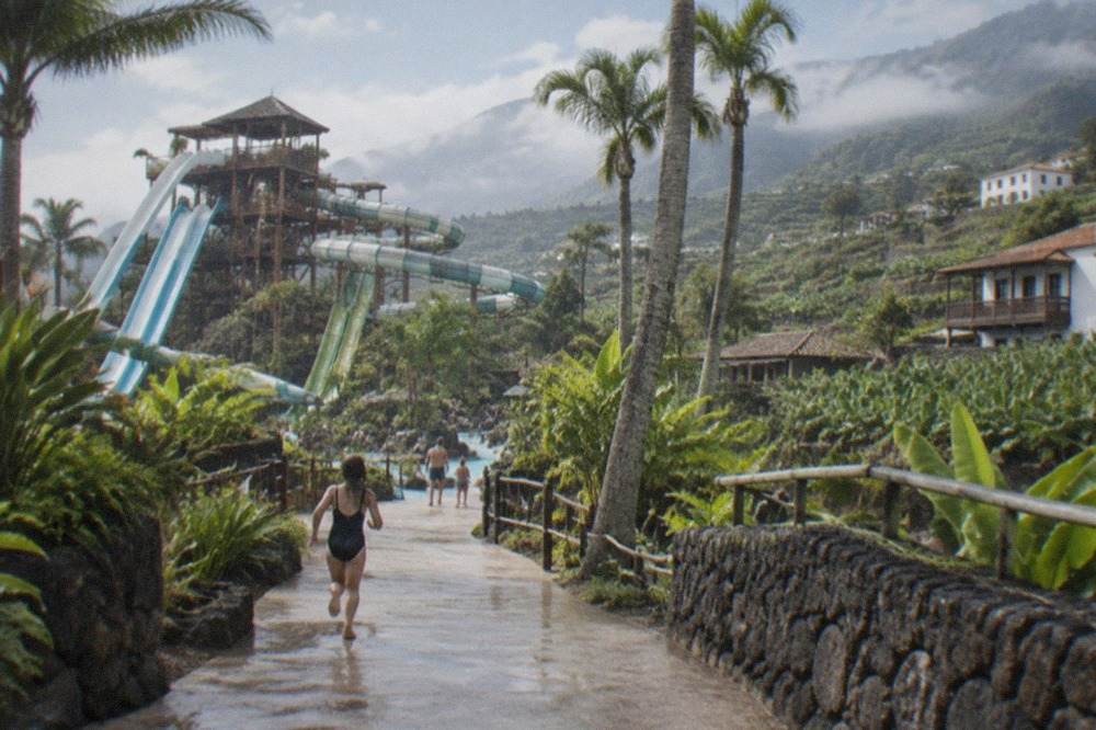 A large tropical water park with a tall slide tower and palm trees under a blue sky