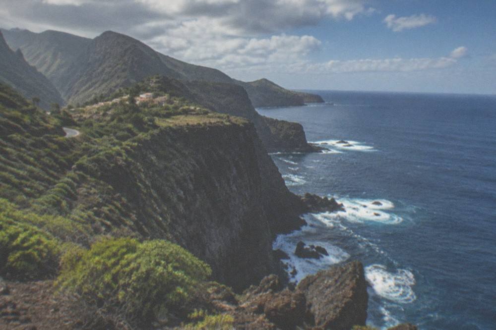 A rocky coastline at Punta de Teno with green shrub and a clear horizon over the sea