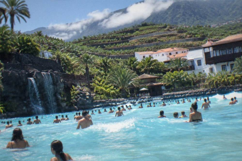 A water park wave pool crowded with swimmers under bright summer sunshine