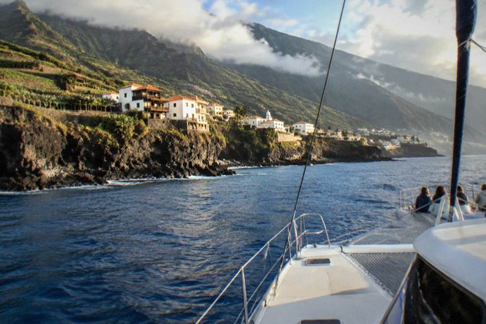 A catamaran sailing on calm blue water near a rocky coastline