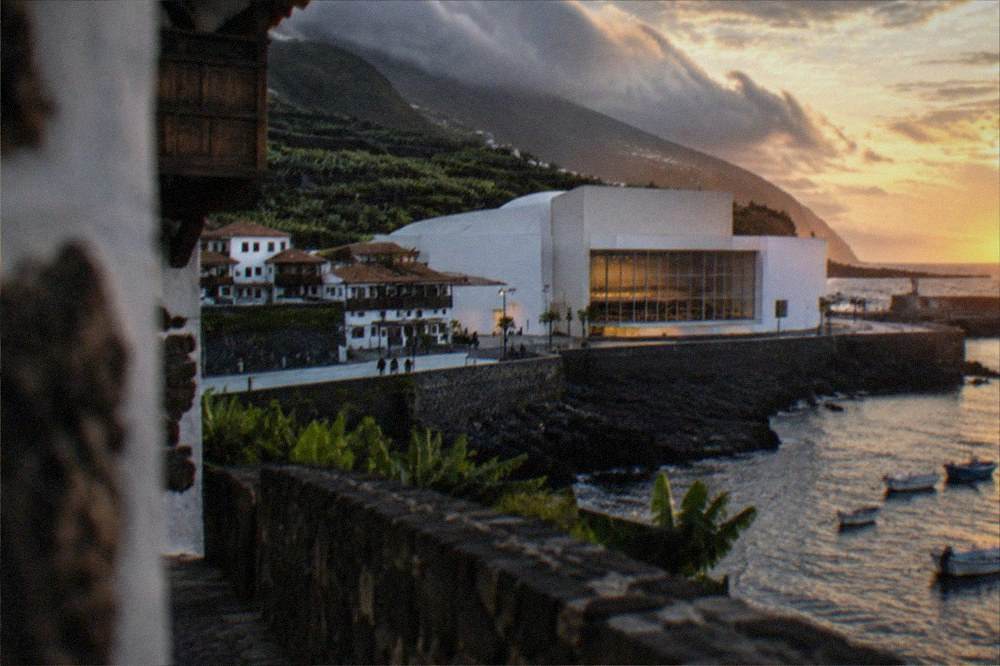 A white concert hall building beside a harbour at dusk