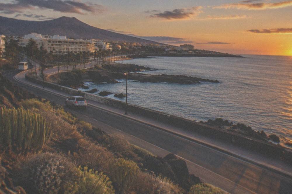 A coastal road at sunset with dark volcanic rocks and calm sea