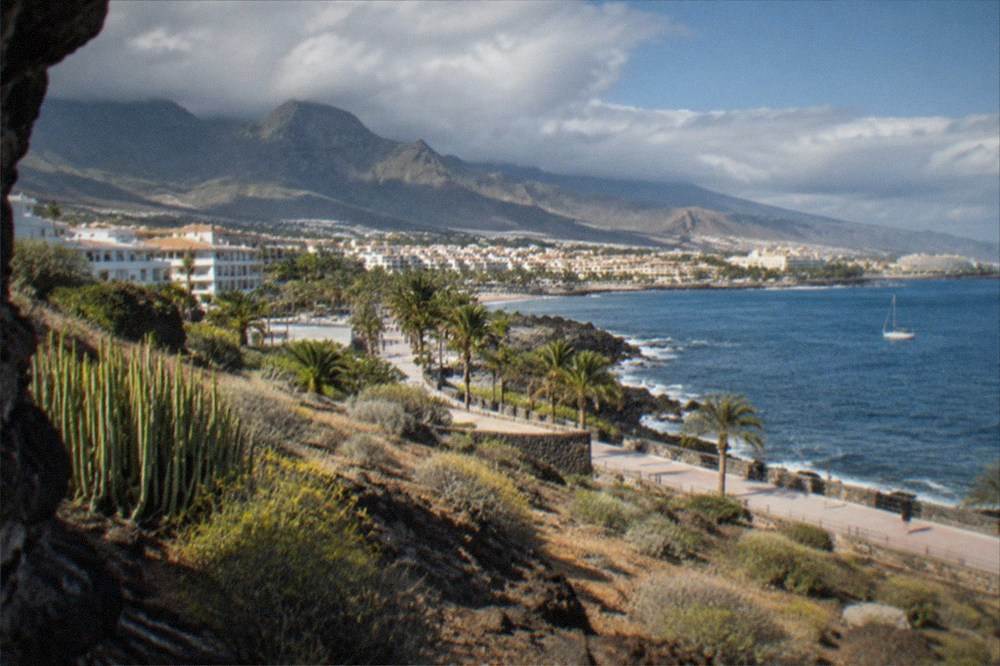 Clouds rolling over green ridges while a coastal town stays in sunshine below