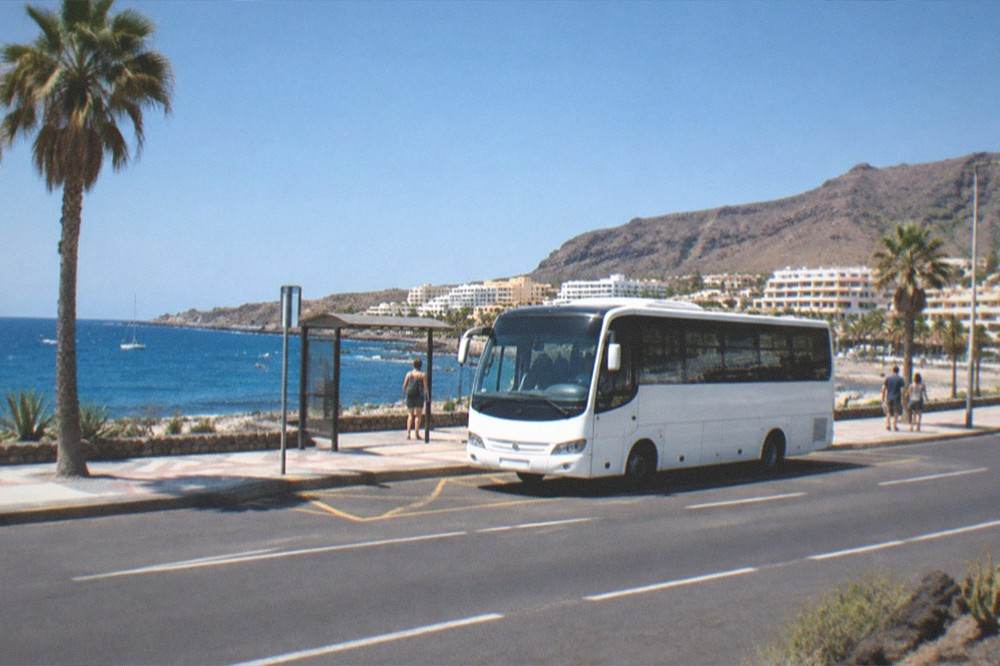 A white island bus waiting at a stop on the coastal road at Los Cristianos