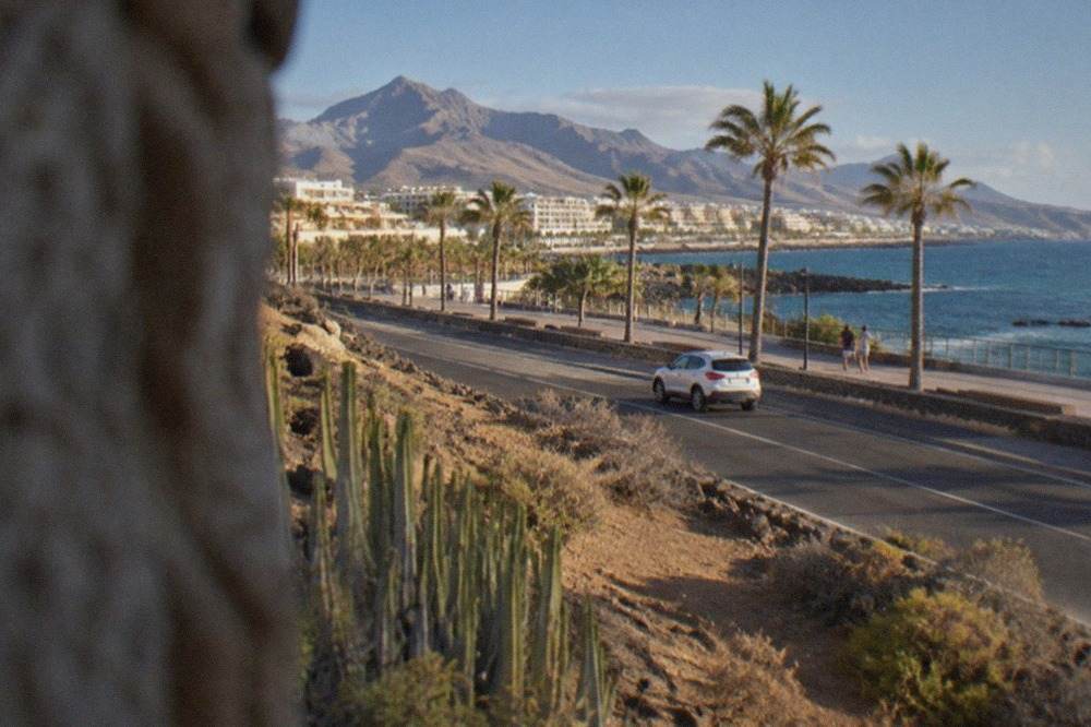 A coastal road through Costa Adeje with palm trees and mountains in the distance under a blue sky
