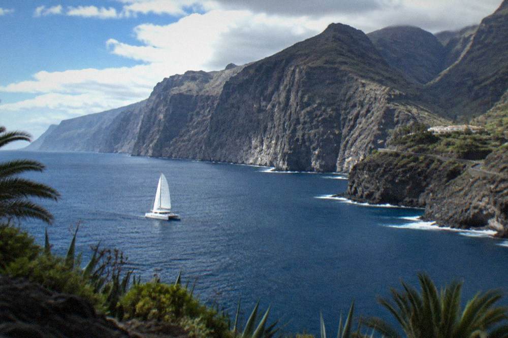 A catamaran under sail on calm blue water near the coast at Los Gigantes