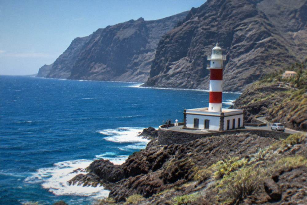 A lighthouse on a rocky point beneath high cliffs at Punta de Teno