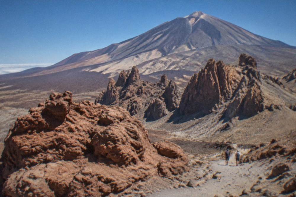 The volcanic cone of Mount Teide rising above reddish rock formations in the national park