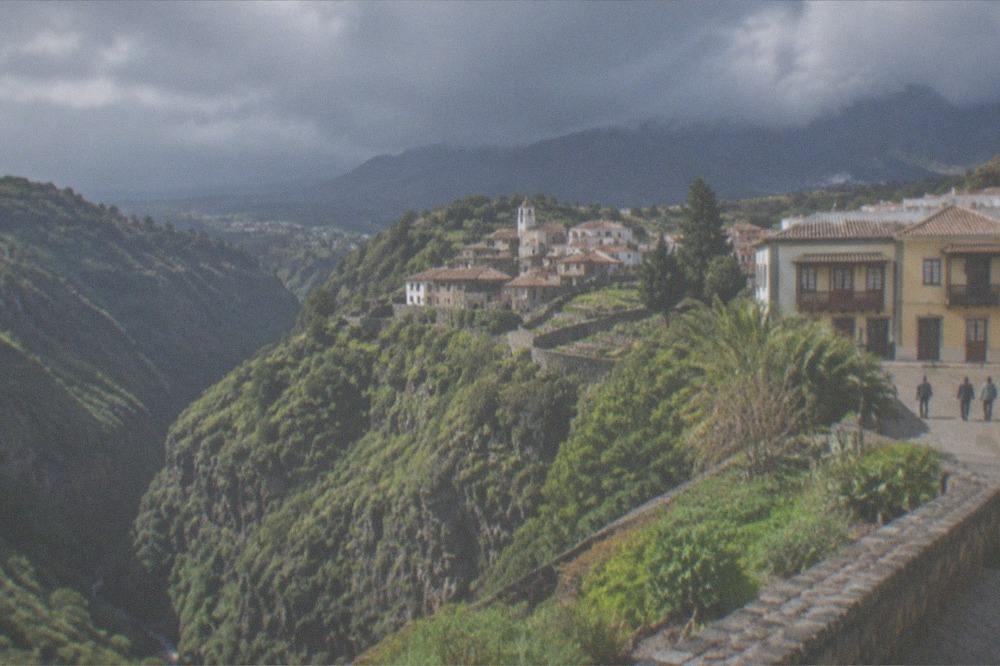 A steep green gorge with a small village of stone houses at its head under rain clouds