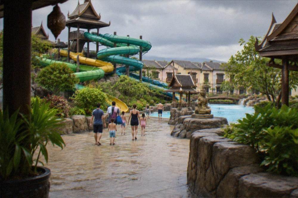 Families walking between water slides in a Thai-themed water park under a cloudy sky