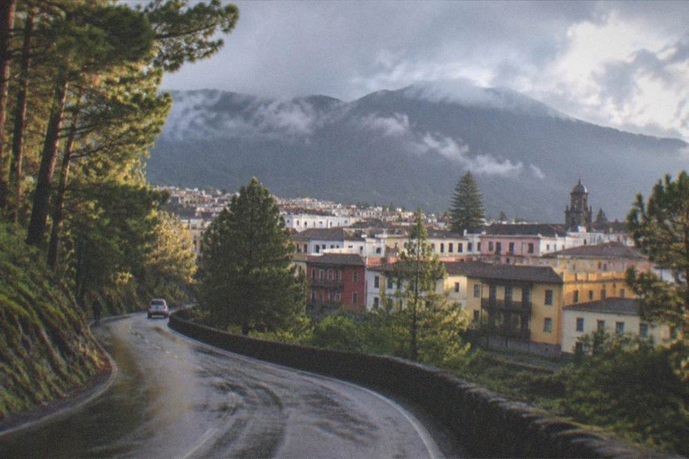 A wet road winding through green pine forest with clouds lifting off the mountains