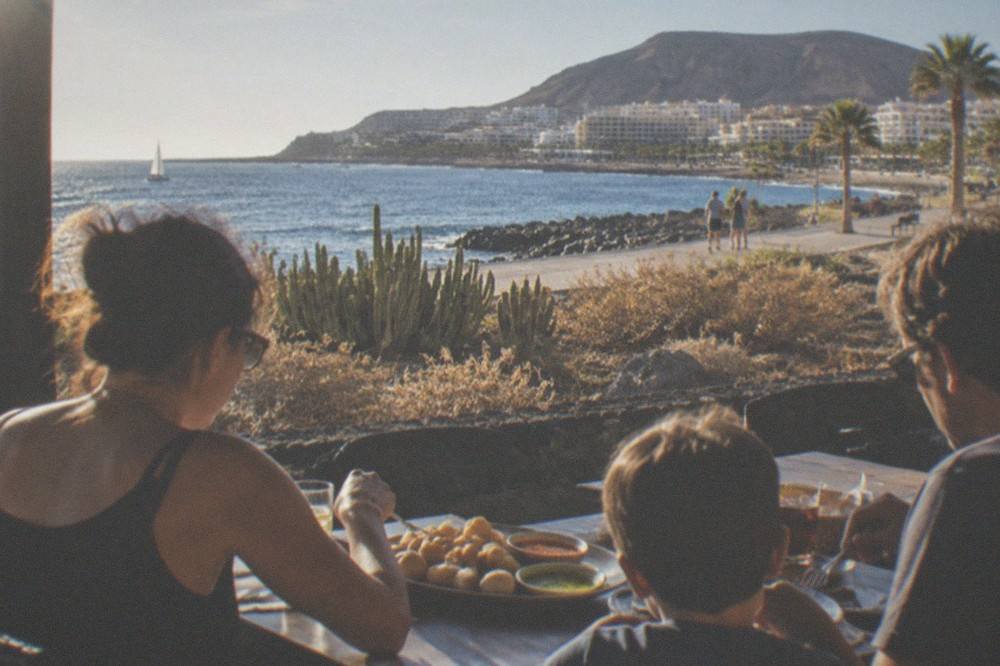 A family sharing a simple lunch of small potatoes with red and green sauces at an outdoor table