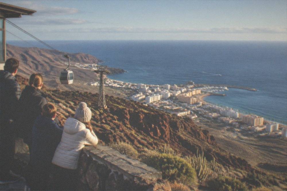 A family in warm jackets looking out over red volcanic rock from a high mountain station above the clouds