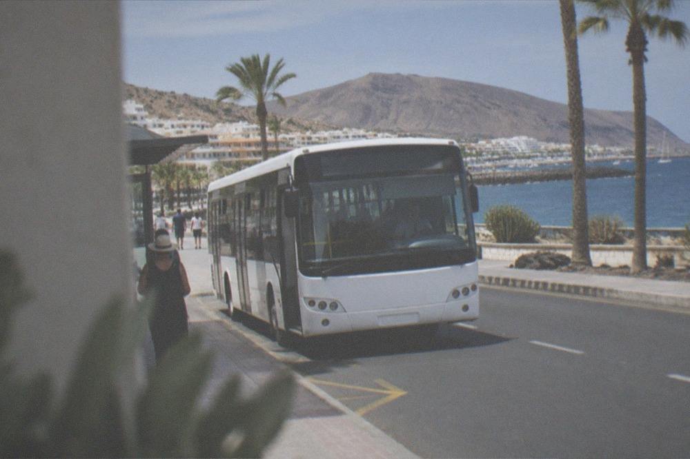 A white island bus pulling into a stop on a sunny Tenerife street