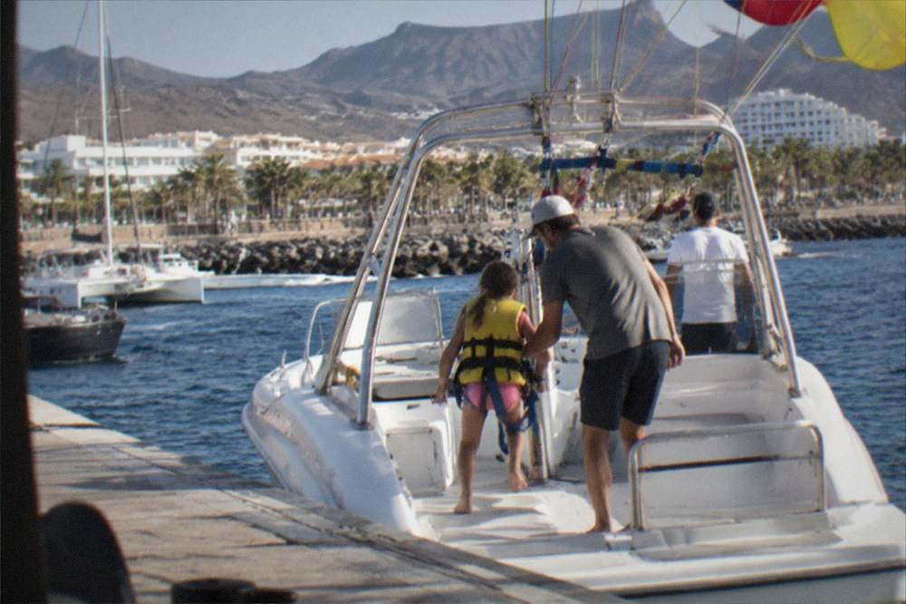 A child being helped onto a parasailing boat at a marina in Costa Adeje