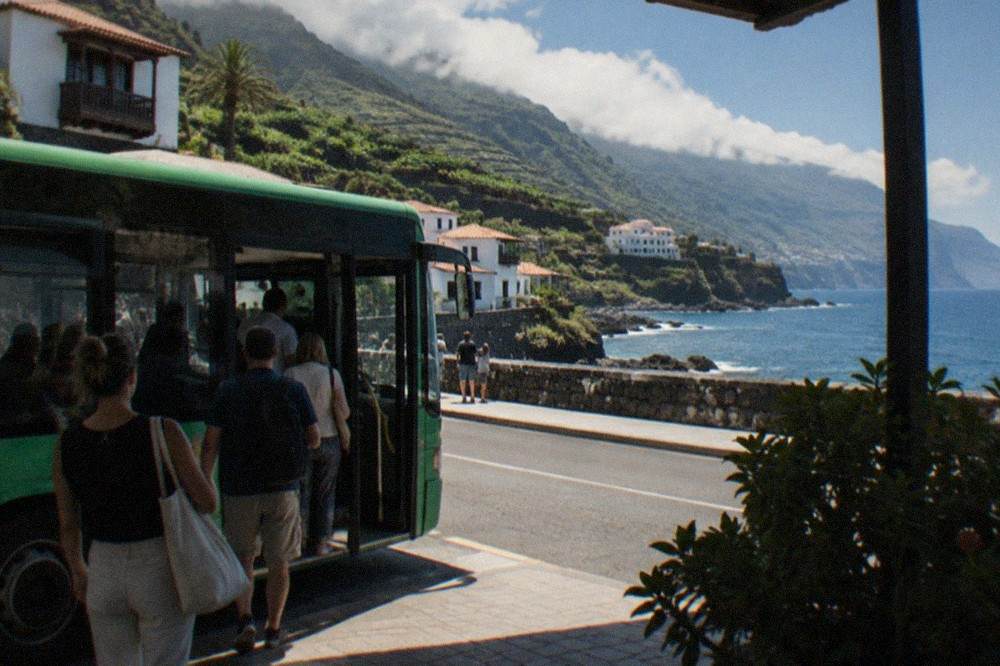 Passengers boarding a green public bus at a seaside stop in Tenerife
