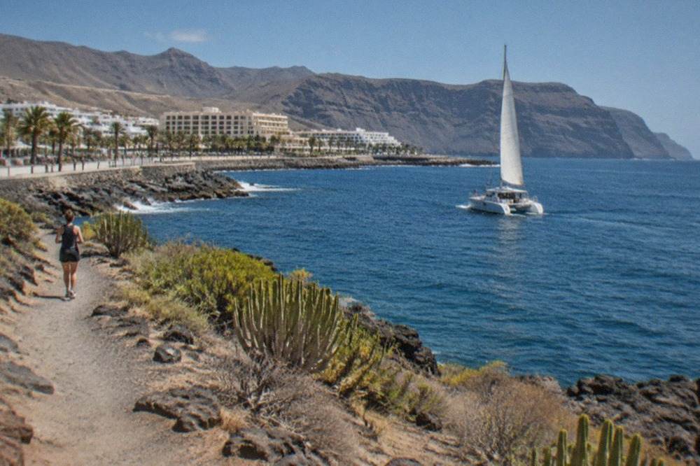 A catamaran sailing on calm blue water off the south coast of Tenerife with cliffs in the distance