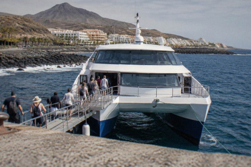 A large catamaran moored at a harbour with passengers boarding