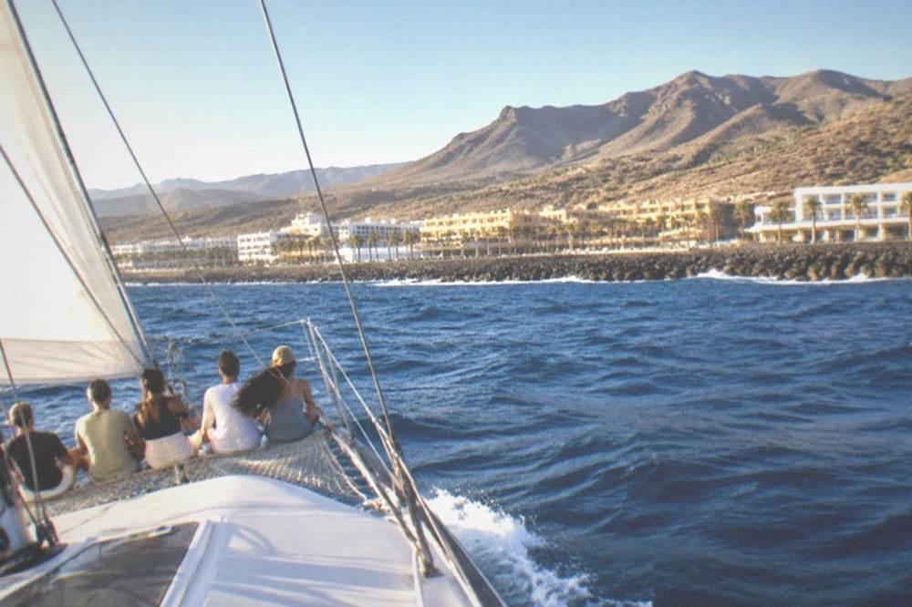 A sailboat heeling in the wind with passengers sitting along the netting at the front