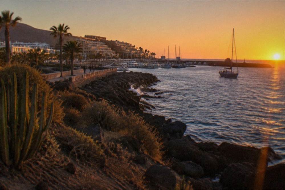 A calm sea at sunset with a boat's mast silhouetted against an orange sky